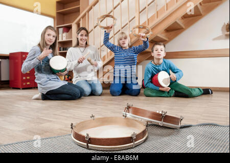 Gruppo di femmina assistente di puericultura e tre bambini drumming Foto Stock