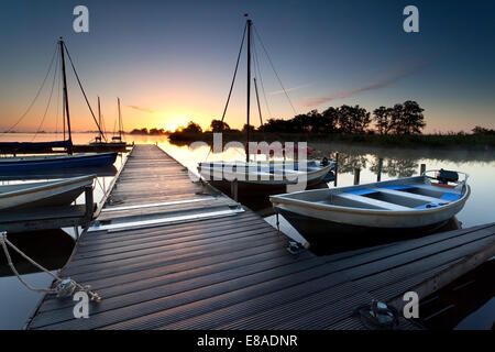 Il molo di legno e barche sul lago grande di sunrise Foto Stock