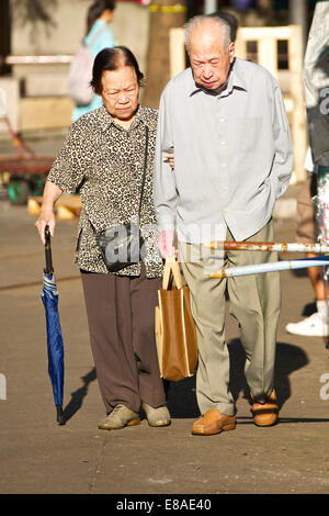 Senior coppia cinese si aiutano a vicenda attraversare la strada a Chun Yeung Street, North Point, Hong Kong. Foto Stock