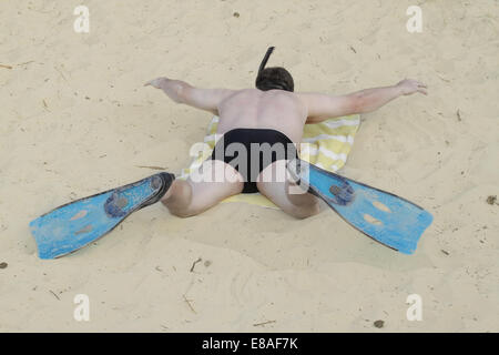 Uomo in pinne e maschera subacquea con snorkel giace sulla sabbia e immagina se stesso floating Foto Stock