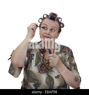 Senior donna si siede con bigodini in i suoi capelli e il colore delle ciglia isolati su sfondo bianco Foto Stock