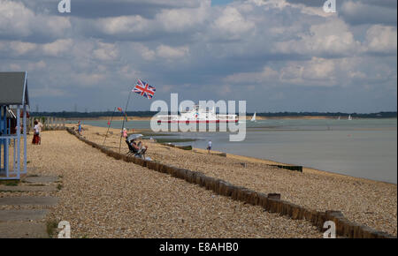 Un Red Funnel passa Calshot spiaggia sul modo per l'Isola di Wight passando cabine sulla spiaggia, battenti bandiera dell'union jack Foto Stock