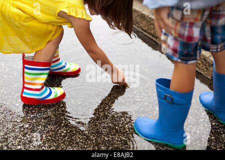 Ragazzo e sorella di indossare stivali di gomma guardando in giù in una pozza di pioggia Foto Stock