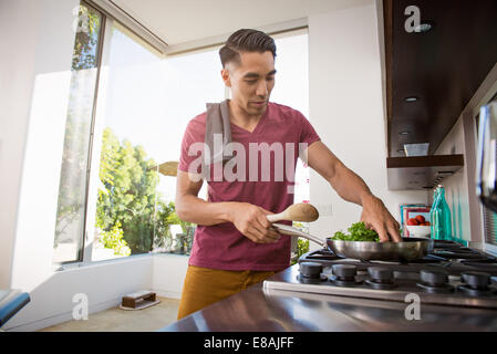 Giovane uomo per la cottura sul piano di cottura in cucina Foto Stock