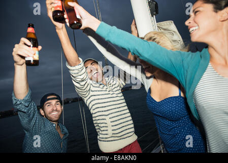 Gli amici la tostatura con bottiglie di birra in barca a vela Foto Stock