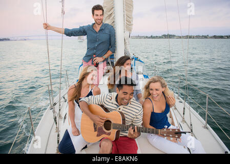 Amici sulla barca a vela, l'uomo a suonare la chitarra Foto Stock