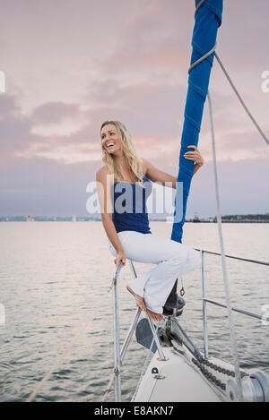 Giovane donna seduta sulla ringhiera in barca a vela Foto Stock