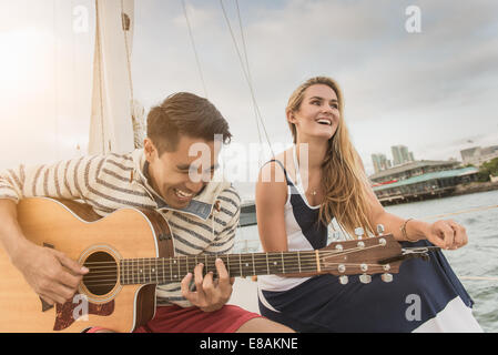 Una giovane coppia in barca a vela, l'uomo a suonare la chitarra Foto Stock