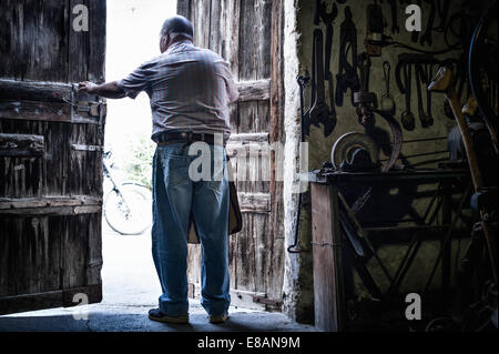 Vista posteriore del maschio anziano fabbro in apertura di sportelli della tradizionale granaio, Cagliari, Sardegna, Italia Foto Stock