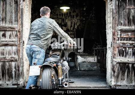 Metà uomo adulto spingendo motociclo nel fienile Foto Stock