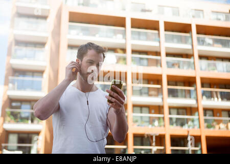 Uomo che ascolta la musica su cuffie, edificio in background Foto Stock
