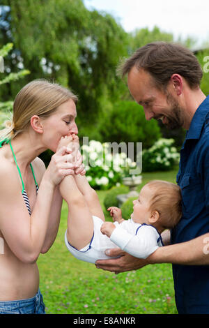 Madre kissing baby figlie in piedi in giardino Foto Stock