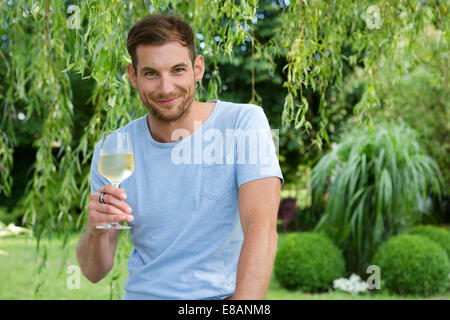 Ritratto di metà uomo adulto tenendo in mano un bicchiere di vino bianco in giardino Foto Stock