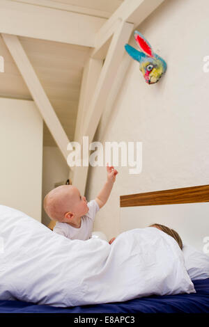 Baby girl rivolta dal letto mentre la madre sotto i coperchi Foto Stock