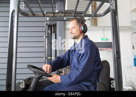 Lavoratore nel carrello elevatore a forche in impianto industriale Foto Stock