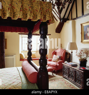 Antico letto a baldacchino intagliati e cassa di legno nella camera da letto del paese con poltrona rosa Foto Stock
