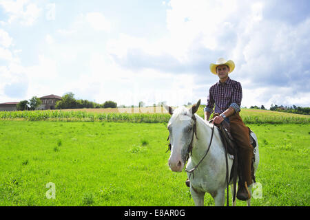 Ritratto di giovane uomo in marcia da cowboy a cavallo nel campo Foto Stock