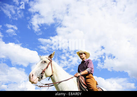 Angolo basso Ritratto di giovane uomo in marcia da cowboy a cavallo Foto Stock