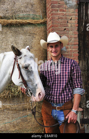 Ritratto di giovane uomo in marcia da cowboy a cavallo fuori stabile Foto Stock