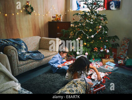 Sorella e fratello gioca con e scartare i regali di Natale sul salotto piano Foto Stock