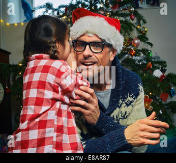 Figlia whispering al padre in santa hat a natale Foto Stock