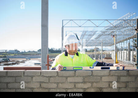 Builder utilizzando la livella sulla costruzione della parete del sito Foto Stock