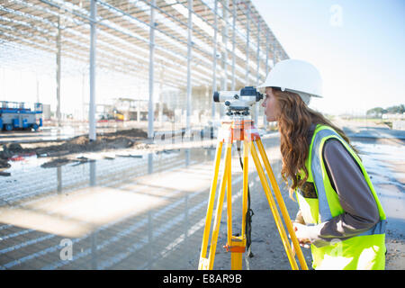 Geometra inclinati in avanti per guardare attraverso il livello sul sito in costruzione Foto Stock