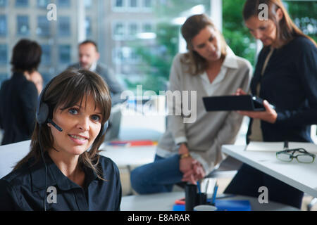 Ritratto femminile di lavoratore di ufficio tramite cuffia telefonica in ufficio occupato Foto Stock