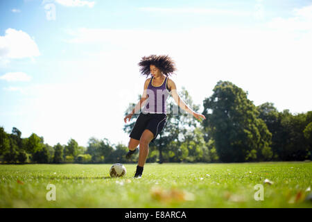 Giovane donna calci palla calcio in posizione di parcheggio Foto Stock