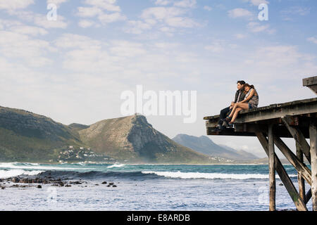 Coppia giovane seduto sul bordo del molo vecchio, Cape Town, Western Cape, Sud Africa Foto Stock