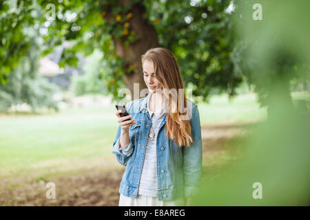 Giovane donna la lettura di testi sullo smartphone in posizione di parcheggio Foto Stock