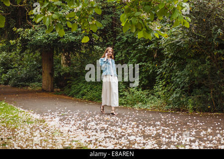 Giovane donna in chat sullo smartphone mentre passeggiando nel parco Foto Stock