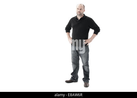 A piena lunghezza shot di un uomo in piedi con le mani sui suoi fianchi cercando perplesso e confuso lontano dalla telecamera e girato in uno studio Foto Stock