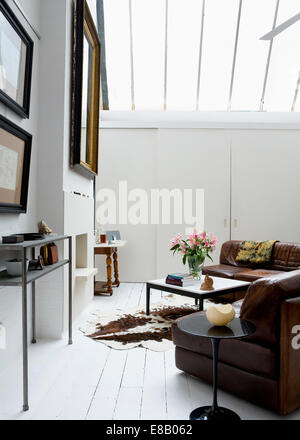Tulip lato tavolo e divani in pelle marrone in bianco moderno salotto con pelle di mucca tappeto sul dipinto di bianco con pavimento in legno Foto Stock