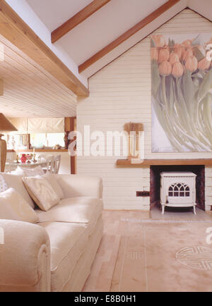 La crema divano in cottage moderno salotto interno con grandi immagini floreali sopra il camino con il bianco stufa a legna Foto Stock