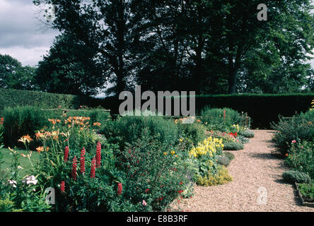 Lupini rosso e arancione hemerocallis in una vasta gamma di piante erbacee confine accanto al sentiero di ghiaia nel paese grande giardino in estate Foto Stock