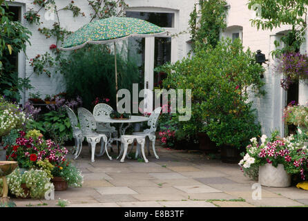 Ombrello verde bianco al di sopra di letti in ferro battuto con tavolo e sedie sul patio con vasi di piante annue colorati Foto Stock