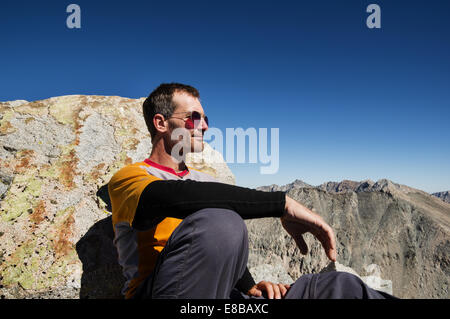 Uomo di mezza età seduto in cima a una montagna appoggiata contro una roccia Foto Stock