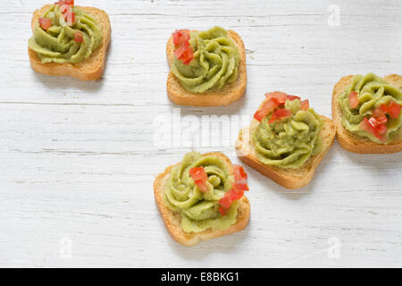 Mini-toast, decorato con il guacamole, pomodoro tagliato a pezzetti, bianco sullo sfondo di legno Foto Stock