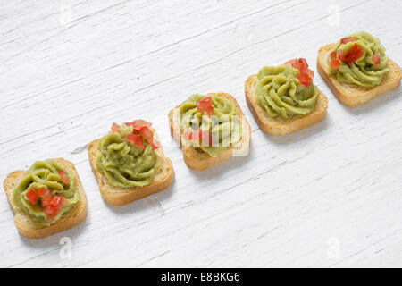 Mini-toast, decorato con il guacamole, pomodoro tagliato a pezzetti, bianco sullo sfondo di legno Foto Stock