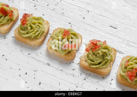 Mini-toast, decorato con il guacamole, pomodoro tagliato a pezzetti, bianco sullo sfondo di legno Foto Stock