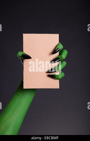 Green monster mano con unghie nere holding pezzo di cartone, tema Halloween Foto Stock
