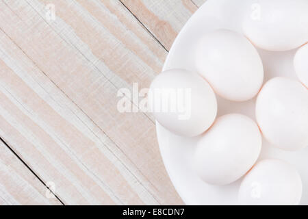 Elevato angolo di visione di un bianco ciotola riempita con le uova bianche su un bianco rustico in legno tavolo da cucina. Formato orizzontale con spazio di copia Foto Stock