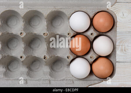 Sei uova, tre bianchi e tre brown, in una grande scatola di cartone con spazi vuoti. La scatola in cartone si trova su un bianco stile agriturismo cucina Foto Stock