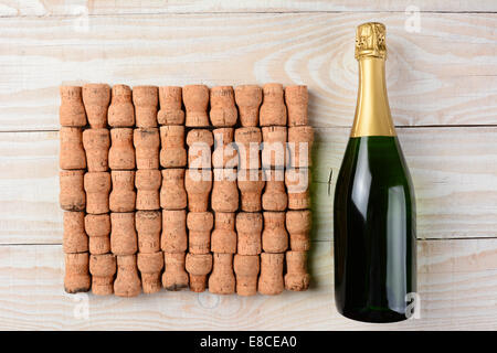 Alta angolazione di una bottiglia di champagne posa accanto ad un grande gruppo di tappi disposti in ranghi su un dipinto di bianco tavola di legno. Foto Stock