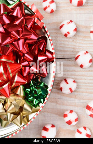 Angolo alto closeup colpo di una lattina rotonda piena di Natale nastri su un bianco tavola di legno con il rosso e bianco conia sparsi. Foto Stock