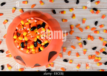 Alta angolazione di una plastica zucca di Halloween riempito con la caramella in un bianco tavola in legno rustico. Formato orizzontale con cereali caramellati Foto Stock