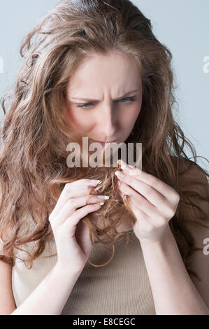 Giovane donna controllando i suoi capelli a doppie punte Foto Stock