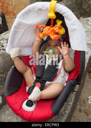 Il bambino gioca con toy giraffa mentre strapped in un sedile di automobile Foto Stock