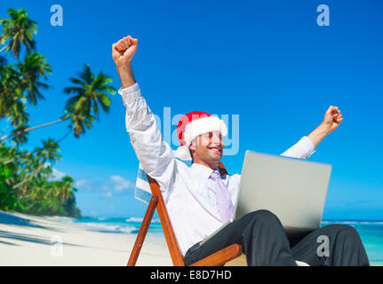 Un imprenditore in un cappello da Babbo Natale e i suoi successi su una vacanza in spiaggia Foto Stock